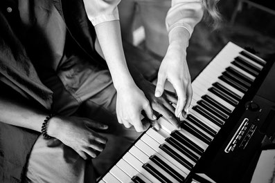 Photo en noir et blanc d'un professeur de piano Suzuki qui replace la main de son élève, un jeune adolescent sur le clavier