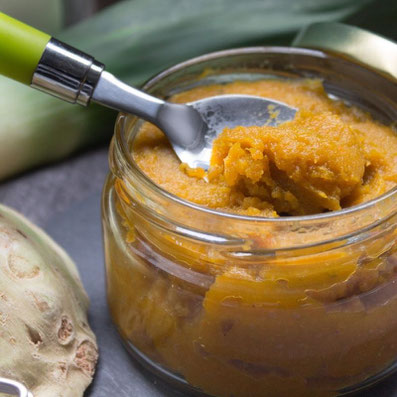 Kleiner Löffel mit orange farbener Paste, im Hintergrund ein Glas mit Paste, eine Stange Lauch und Knollensellerie