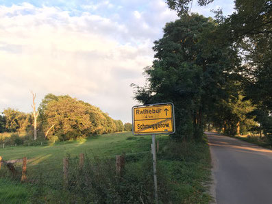 Blick über eine Wiese und im Vorderung das Ortsausgangsschild von Schmuggerow