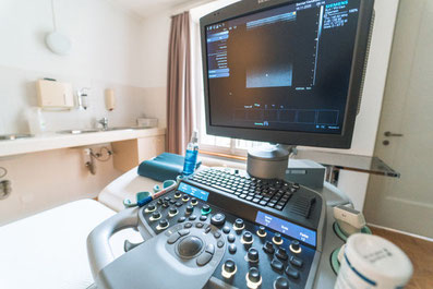 Ultraschallgerät im Fokus, im Hintergrund Patientenliege in Praxisraum