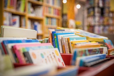 Bücher sind in Kisten gestapelt, im Hintergrund sind unscharf volle Bücherregale zu erkennen