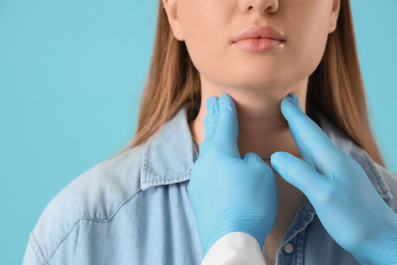 Ärztin berührt Hals einer Patientin mit den Händen und blauen Handschuhen