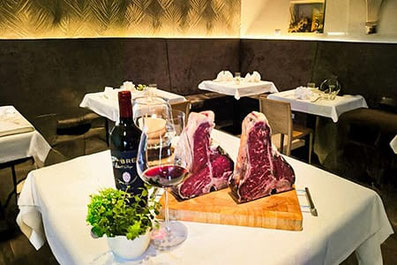 Eleganter Tisch im Restaurant Gries 13 in Bozen mit zwei Fiorentina-Steaks, Rotwein und Glas – stilvolle Atmosphäre im Weinbistro während der Fiorentina-Wochen.