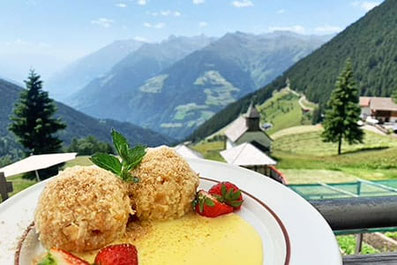 Hausgemachte Südtiroler Knödel mit Vanillesauce, serviert vor einer atemberaubenden Berglandschaft im Gasthaus Haashof in Schenna.