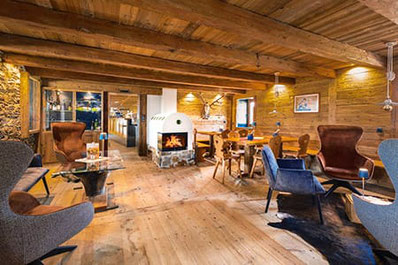 Gemütliche Stube der Starkenfeldhütte mit Holzdecke, Kaminfeuer, rustikalen Holztischen und modernen Sesseln – perfekte Mischung aus alpinem Charme und Komfort.