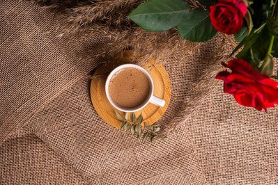 麻のテーブルクロスの上に置かれたコーヒーのマグカップ。傍らに真っ赤なバラの花。