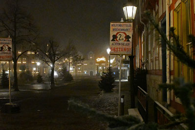 Das wolfenbütteler Stadtmarkrt im Nebel. Schilder mahnen dazu, Abstand zu halten. Die Bäume auf dem Platz sind weihnachtlich geschmückt. Der Platz liegt im Nebel.