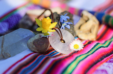 Anden-Zeremonie mit buntem Inka-Tuch, Heilsteinen, Blumen und Rosenquarz-Amulett auf einer schamanischen Altardecke.