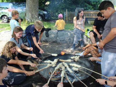 Jugendgruppe macht Stockbrot am Lagerfeuer - auch über dem Feuer möchten wir in diesem Ferienlager gemeinsam kochen