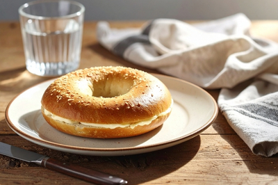 バターがサンドされたベーグルパンのお皿。水の入ったグラス。キッチンクロス。