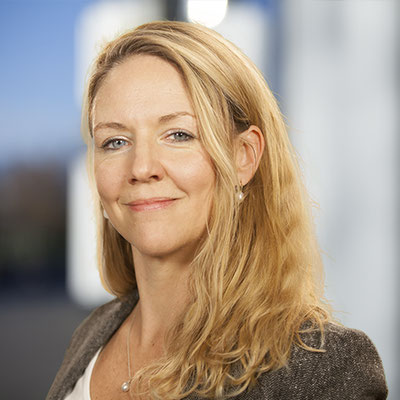 Portrait von Aimée Bastian, Systemischer Coach, Kinder- und Jugendcoach, auf einem blauen architektonischen Hintergrund.