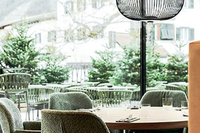 Ristorante elegante con moderne poltrone verdi, tavolo in legno coperto e vista sulla terrazza con abeti e facciate della città nel ristorante Soley di Bressanone.