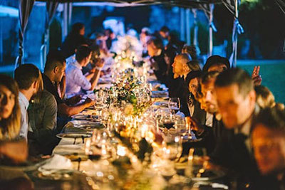 Elegantes Dinner-Setting bei Nacht mit festlich gedecktem Tisch und Gästen, die eine unvergessliche Veranstaltung genießen – Catering-Service von Hannah & Elia.