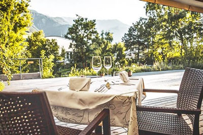 LA VIMEA Vegan Restaurant in Naturns: Stilvoll gedeckter Tisch auf der Terrasse mit Blick auf Garten und Vinschger Bergwelt – veganer Gourmetgenuss.