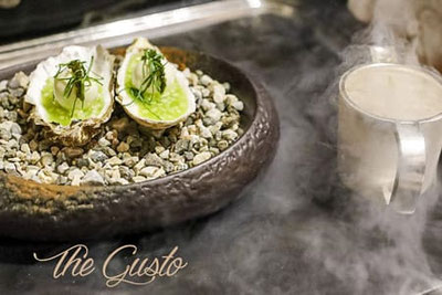 Gourmetgericht beim The Gusto Festival im Romantik Hotel Stafler: Austern serviert auf Kieselsteinen mit Kräutern, begleitet von einem dampfenden Getränk.