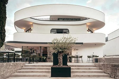 Moderno edificio sinuoso del Soley Suites Hotel - Adults only a Bressanone con terrazza e ulivo: il design elegante incontra il fascino mediterraneo nel cuore dell'Alto Adige.