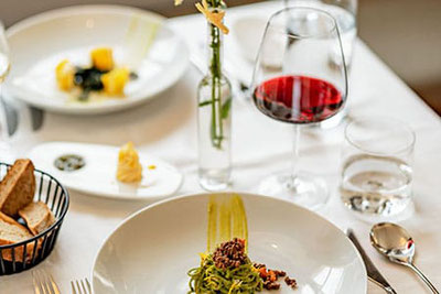 Fein angerichtete Pasta mit Löwenzahn, dazu ein Glas Rotwein – Genussvoller Frühlingstisch im Rahmen der Löwenzahnwochen am Deutschnonsberg in Südtirol.