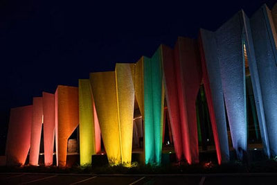 Facciata illuminata della Cantina Kurtatsch di notte: lamelle in calcestruzzo dai colori dell'arcobaleno risplendono suggestivamente durante l'evento “Aperitivo Panoramico” in Alto Adige.