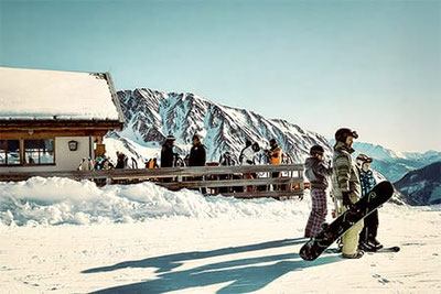Sciatori e snowboarder davanti al rifugio Lazaunhütte nella Val Senales, terrazza soleggiata in inverno, montagne innevate e panorama alpino sopra Maso Corto.