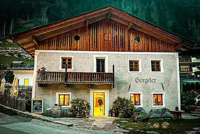Gorgeler Bar & Steakhouse in Ratschings: traditionelles Haus mit Holzfassade, Balkon und warm beleuchtetem Eingang in alpiner Umgebung am Abend