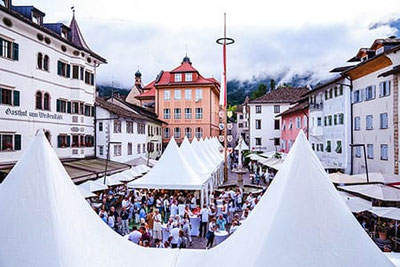La piazza di Caldaro durante l'evento “Caldaro in abito bianco”, con tendoni allestiti a festa e una grande folla che degusta e assapora i migliori vini bianchi di Caldaro. 