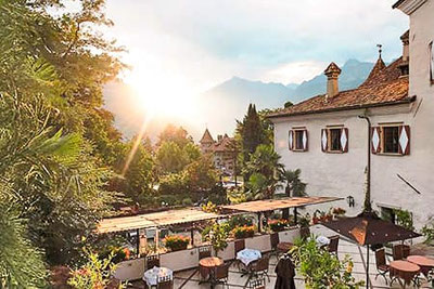 Romantische Terrasse des Restaurants Castel Rundegg in Meran mit Blick auf Berge und Garten – perfekter Ort für Dinner bei Sonnenuntergang in Südtirol.
