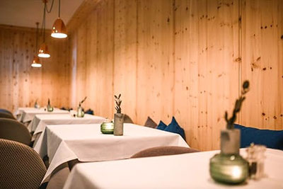Gemütlicher Gastraum mit Holzvertäfelung, weiß gedeckten Tischen und warmem Licht im Adlernest Bistro in Unser Frau im Schnalstal.
