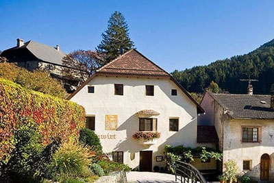 Ristorante Turmwirt a Gudon, edificio storico con facciata bianca, balcone fiorito e ponticello, immerso tra vigneti e paesaggio autunnale.