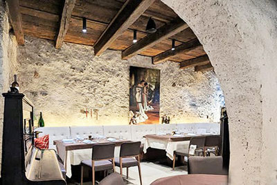 Sala storica del ristorante Festival Merano con pareti in pietra naturale, soffitto in legno, opere d'arte moderna e tavoli apparecchiati in un'atmosfera elegante e accogliente.