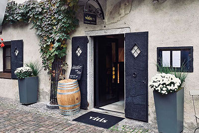 Ingresso dell'enoteca Vitis a Bressanone: ambiente elegante con porta in pietra scura, botti di vino, decorazioni stagionali e un affascinante cortile interno nel cuore del centro storico.