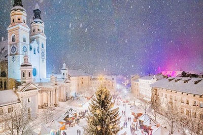 Stimmungsvoller Brixner Weihnachtsmarkt am Domplatz mit festlich geschmücktem Christbaum, Lichtern und Schneefall – weihnachtliche Atmosphäre in Südtirols ältester Stadt.