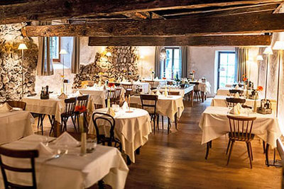 Elegantes Restaurant im Rössl Bianco in Meran mit stilvollem Ambiente, rustikalen Steinwänden, Holzbalkendecke und liebevoll gedeckten Tischen – ideal zum gut essen in Meran.