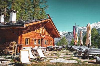 Holzalm auf 2.015 m mit Sonnenliegen, Bergblick auf die Ötztaler Alpen, Terrasse mit Sitzplätzen, Lärchenwald, blauer Himmel, Lafetz Alm im Schnalstal