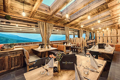 Vista sulla sala da pranzo del ristorante Ban Rutzner a S. Andrea, vicino a Bressanone, con molti mobili in legno naturale e una splendida vista sulle montagne circostanti.