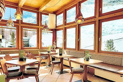 Heller Wintergarten im Restaurant Rosmarie in Pfelders mit Holztischen, großen Fenstern und Blick auf die verschneite Berglandschaft im Passeiertal.