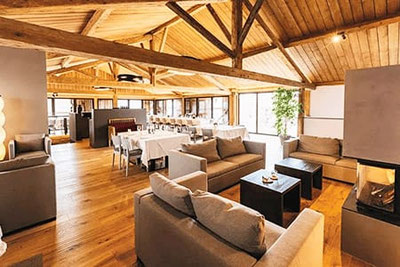 Gemütlicher Gastraum im Berggasthof Dorfner in Montan mit Holzbalkendecke, Kamin, Loungeecke und stilvoll gedeckten Tischen – ideal für Feiern und Hochzeiten.