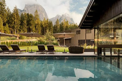 Beheizter Außenpool mit Liegen und Sonnenschirmen im Waldrast Living in Seis am Schlern, mit Blick auf Wald und die beeindruckenden Dolomiten der Seiser Alm