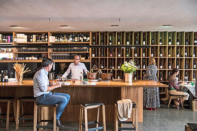 Vinzenz - zum feinen Wein, – Ristorante & wine bar a Vipiteno: elegante bancone in legno, selezione di vini in vetrina, ospiti intenti a degustare vini pregiati e prelibatezze.