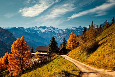La malga Prantneralm sopra Vipiteno nella Alta Valle Isarco in Alto Adige con boschi di larici dorati, vista panoramica sulle Alpi dello Stubai innevate e idilliaco sentiero alpino.