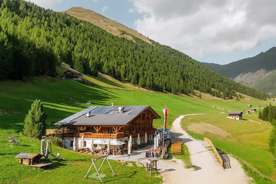 Vista sulla Großberghütte nella Valle di Altafossa con terrazza soleggiata, circondata da prati alpini e montagne, ideale per gustare specialità regionali e piatti tipici di malga.