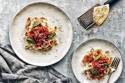 Ultner Genuss im Ultental: Hausgemachte Tagliatelle mit Tomatensauce, Basilikum und Parmesan stilvoll auf rustikalem Tisch serviert.