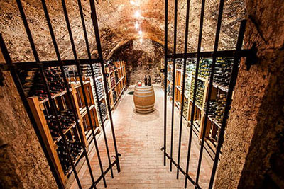 Cantina storica con scaffali in legno, bottiglie di vino e botti sulla Strada del Vino dell’Alto Adige.