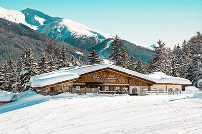 „Restaurant Jora Mountain Dining in San Candido, umgeben von verschneiten Bergen, bietet eine rustikale Atmosphäre und ist bekannt für exklusive Events wie 'Pasta on the Rocks'.”