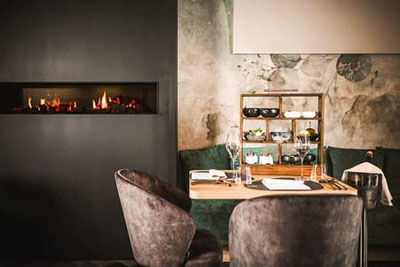 Stilvoll gedeckter Tisch im Restaurant SomVino in Dorf Tirol mit Kamin, eleganten Sesseln und warmem Licht, modernes Ambiente für genussvolle Abende
