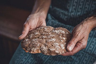 Il tradizionale pane Paarl della Val Venosta è tenuto dalle mani di una contadina – simbolo della festa del pane Pavicolo Storie di pane a Lana, Alto Adige.