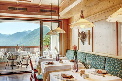 Helle Tiroler Stube im Restaurant Sonne Dorf Tirol mit Panoramablick auf Meran, stilvoll gedeckte Tische, Holzinterieur und gemütliche Atmosphäre