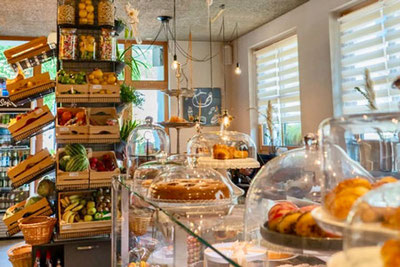 Innenansicht des Stabner Postlodn mit frischem Obst, Gebäck unter Glasglocken und liebevoll gestaltetem Verkaufsraum – Mischung aus Café, Bar und Feinkostladen.