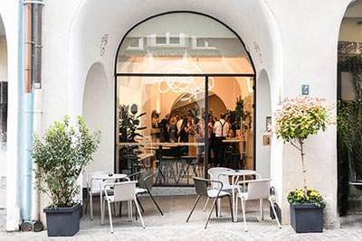 Außenbereich des Arcus Bar & Café in Meran mit Tischen unter den historischen Lauben, stilvollem Ambiente und Blick in das moderne Café im Stadtzentrum.