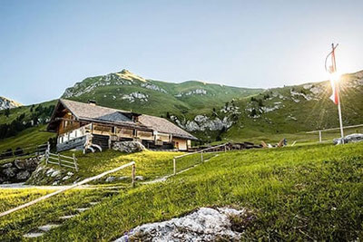 Die Gampenalm in Villnöss bei Sonnenaufgang, umgeben von grünen Almwiesen und Bergen – beliebtes Ausflugsziel mit Hütte und Blick auf die Dolomiten.