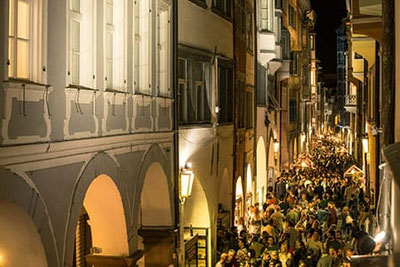 Folla durante i Calici di Stelle a Bolzano sotto i portici storici di notte con stand di vino e illuminazione suggestiva.